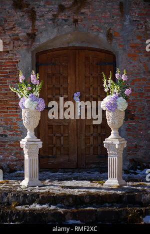 Des pots de fleurs décorés d'argile blanche avec un bouquet de printemps pastel d' hortensias positionnés de chaque côté d'une porte en bois vintage Banque D'Images