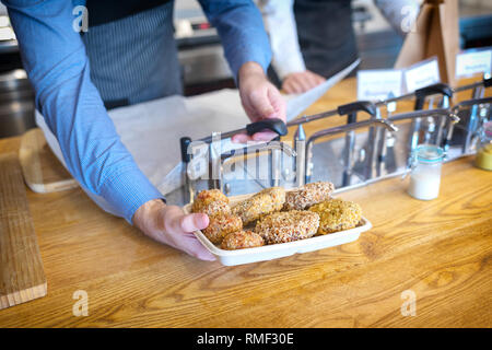 Déjeuner à emporter concept avec l'ajout de serveur dans la sauce sur les boulettes de fast food restaurant pour client, man hand holding en casserole remplie d meatba boulangerie Banque D'Images