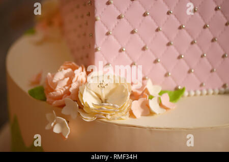 Close up de glaçage délicat décor floral sur un gâteau à plusieurs niveaux, orné de rose pastel velours cerise, fleurs de sucre et d'argent bijoux comestibles Banque D'Images