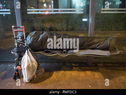 Déposée - 08 février 2019, Hessen, Frankfurt/Main : 08.02.2019, Hessen, Frankfurt/Main : enroulé dans un sac de couchage, ses affaires sur un chariot sac à côté de lui se trouve une personne sans-abri dans un arrêt de bus dans le Westend. Bon nombre des "clients" des bus de la réfrigération ont leurs lieux réguliers, qui sont visités, nuit après nuit par les employés de la Frankfurter Verein. (Zu dpa ''Vous êtes des anges - Frankfurt bus froid on tour' à partir de 13.02.2019) Photo : Boris Roessler/afp Photo : Boris Roessler/dpa Banque D'Images