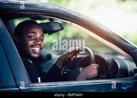 African business man driving et souriant tout en restant assis dans une voiture avec ouvrir la fenêtre avant. Banque D'Images