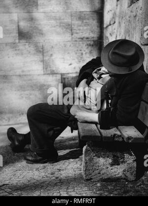 Un homme avec un chapeau et bouteille dort sur un banc. Banque D'Images