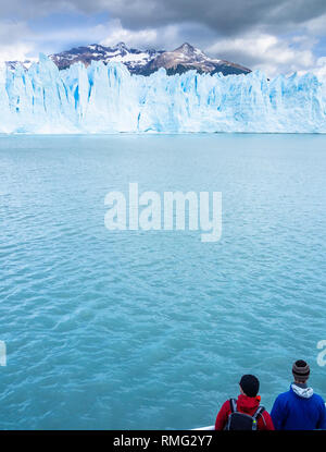 Vue arrière de deux touristes admirant le calme de la mer froide et spectaculaire falaise de glace par jour nuageux en Argentine Banque D'Images