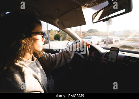 Vue latérale des jeunes femmes élégantes holding hand sur volant en conduisant voiture moderne on city street sur sunny day Banque D'Images