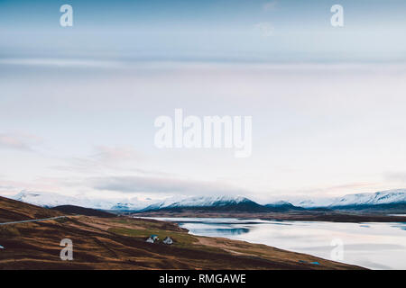 Village avec fermes dans une zone rurale des montagnes d'Islande, avec les montagnes enneigées en arrière-plan. Banque D'Images