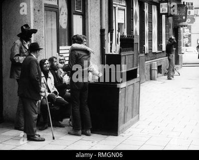 Les jeunes s'asseoir devant leur propre maison bar dans Occamstrasse dans le quartier de Schwabing à Munich, à laquelle des bougies brûlent. Un vieux passant examine de plus près ce qui se passe. Banque D'Images