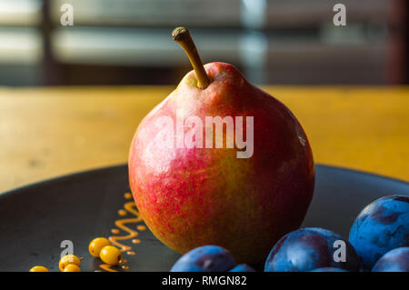 Still Life - prunes juteuses, grand bleu, de poire mûre et de petits fruits de l'argousier dans une plaque en céramique sur un fond de bois, close-up Banque D'Images