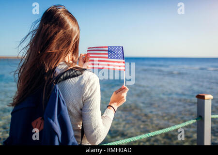 Young Woman admiring paysage de mer rouge et holding USA drapeau sur la jetée. Concept de voyage. Date de l'indépendance d'Amérique Banque D'Images