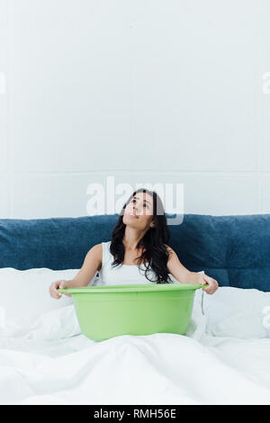 Contrarié brunette woman sitting on bed et retenue d'eau Banque D'Images