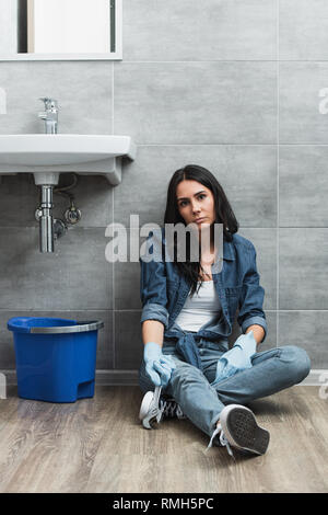 Tired woman sitting on floor avec clé dans la salle de bains Banque D'Images