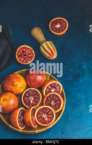 La moitié d'orange sanguine de Sicile et pressé pressé couper dans la plaque de bois béton sur bleu foncé surface de la table. Style rustique foncé. Banque D'Images