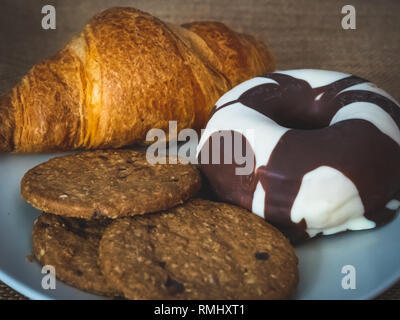 Une plaque avec un croissant, un beignet au chocolat et des cookies sur un fond de toile vintage Banque D'Images