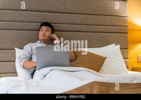 Asian businessman en utilisant le téléphone de la chambre d'hôtel Banque D'Images