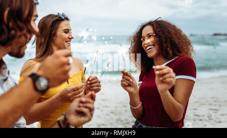 Divers groupes de jeunes amis célébrant le jour de l'an à la plage. Groupe d'hommes et femmes d'avoir du plaisir avec les cierges magiques en plein air sur la plage. Banque D'Images