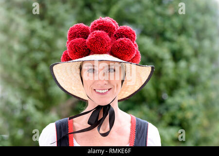 Belle jeune femme portant un Bollenhut traditionnel de la Forêt Noire, avec ses pompons 14 comme elle sourit à l'appareil photo à l'extérieur contre verdure Banque D'Images