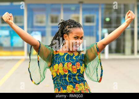 Belle vivacité African American girl clameurs et de rire et le poinçonnage de la sir avec son poing qu'elle célèbre en plein air Banque D'Images