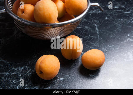 Organique mûres les abricots dans une passoire en acier. Composition dans un style rustique - jaune bio abricots juteux dans son ensemble et passoire en acier et des moitiés d'abricots o Banque D'Images