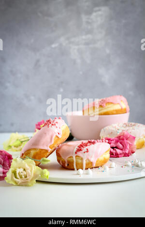 Une pile de donuts rose avec des fleurs sur fond sombre Banque D'Images