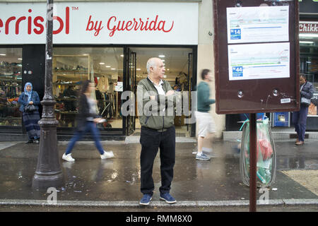 L'homme en attente à l'arrêt de bus temporaires que les piétons marchent par, Boulevard Barbès, Paris, France Banque D'Images