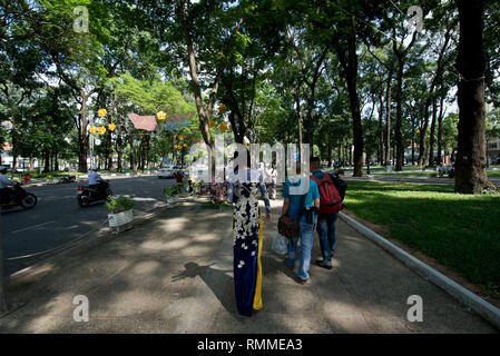 Personnes marchant dans le parc, avec une femme dans le traditionnel Ao Dai vêtue marchant par les touristes, parc près de la cathédrale notre Dam, Ho Chi Minh ville (HCMC), Vietnam Banque D'Images