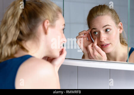 Au cours de l'épaule d'une belle jeune femme inquiète au vieillissement tout en regardant dans le miroir à la peau autour des yeux Banque D'Images