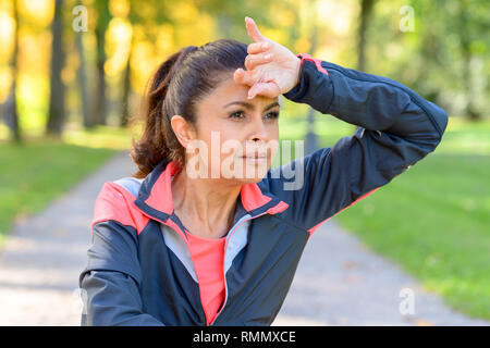 Woman wiping son front avec le dos de sa main tandis qu'elle reprend sa course à l'extérieur dans un parc à la recherche sur le côté avec une expression grave Banque D'Images