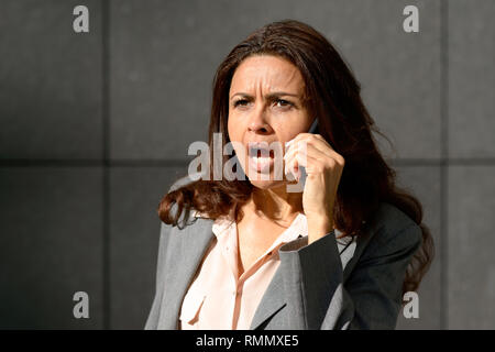 Femme parlant affectif sur son téléphone portable en parlant fort avec une expression frustrée qu'elle fait de son point Banque D'Images