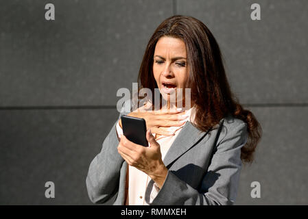 Choqué femme d'âge moyen de la lecture d'un message texte sur son téléphone mobile avec une expression de stupeur Banque D'Images