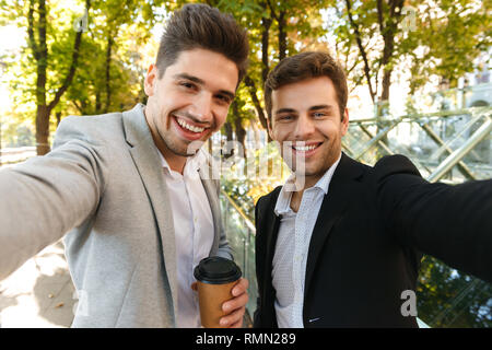 Photo de portrait d'hommes d'affaires en costumes prendre photo sur smartphone selfies en plein air tout en marchant à travers le parc vert avec du café à emporter Banque D'Images