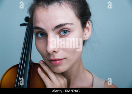 Portrait d'une belle jeune femme posant avec un violon isolé sur fond bleu Banque D'Images