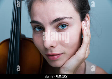 Portrait d'une belle jeune femme posant avec un violon isolé sur fond bleu Banque D'Images