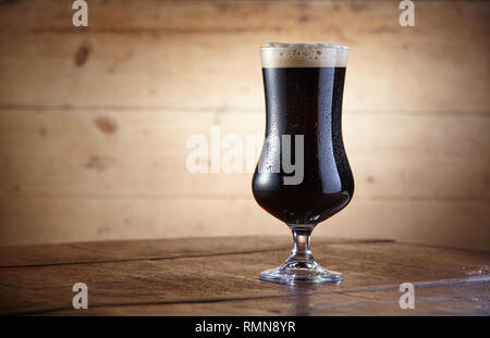 Gobelet en verre de bière stout froid debout sur le tableau contre fond de bois Banque D'Images