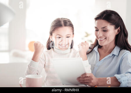 Très excitée. Sweet-talent face fille d'énergie pendant l'exécution d'un projet scolaire innovateur avec son sourire mère utile Banque D'Images