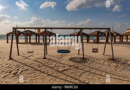 Une plage de sable déserte à Tel Aviv, Israël, avec des balançoires et des pavillons. Banque D'Images