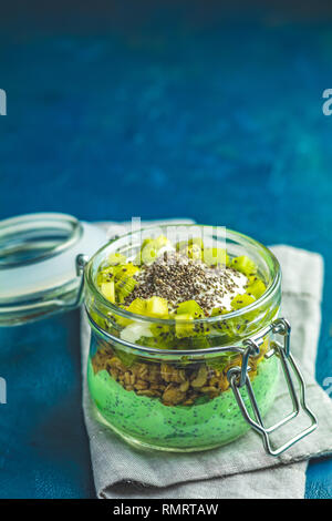 Semences Chia pudding avec le thé vert matcha, kiwi et granola en verre sur fond de béton bleu foncé. Petit déjeuner sain. Banque D'Images