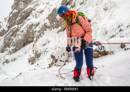 Jeune fille en rappel un rocher abrupt dans un étroit couloir couvert de neige fraîche, à l'aide d'un tube plaque d'assurage, sauvegardés avec une friction prusik noeud sur un 7. Banque D'Images