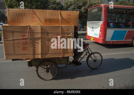 Chinese man riding un tricycle cargo chargés de marchandises emballées dans du carton dans une rue de la Chine. Les vélos-cargos de marchandises ou les tricycles sont populaires transpor Banque D'Images