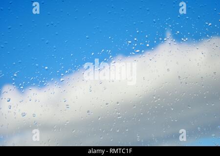 Fenêtre avec des gouttes de pluie contre un ciel bleu avec des nuages blancs après une tempête au milieu de l'hiver. Changement de temps.Le temps efface.Les gouttes de stick à la fenêtre Banque D'Images