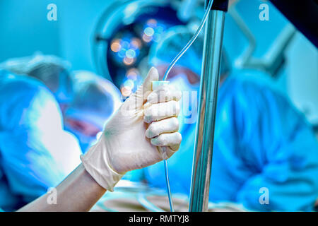 Compte-goutte dans une veine close-up sur un arrière-plan de l'approche chirurgicale opérationnelle. Femme médecin dans gants stériles définit le goutte-à-goutte Banque D'Images