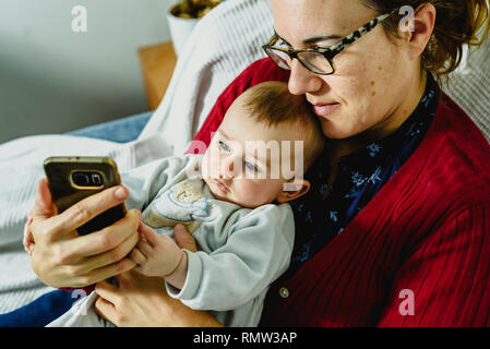 Bébé sur le bras de sa mère en train de jouer avec un téléphone mobile pour explorer le monde virtuel. Banque D'Images