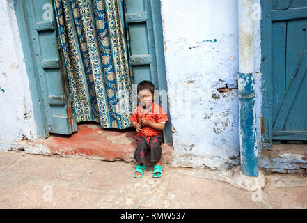 AGRA, Uttar Pradesh, Inde - février 24, 2015 : Petite jeune Indien assis près de sa maison à la porte étroite rue de Taj Ganj district. Banque D'Images