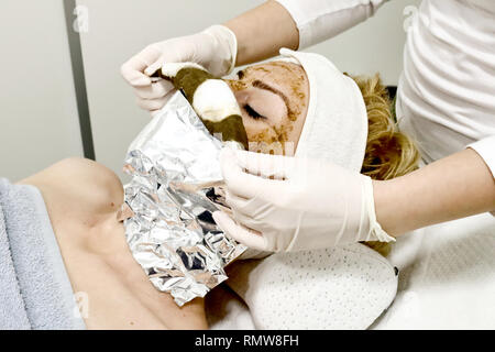 Travailleur esthéticienne dépose le masque facial cosmétique de mer ​​Algae pour la lutte contre le vieillissement et l'hydratation de la peau des femmes client en instituts de beauté close up Banque D'Images