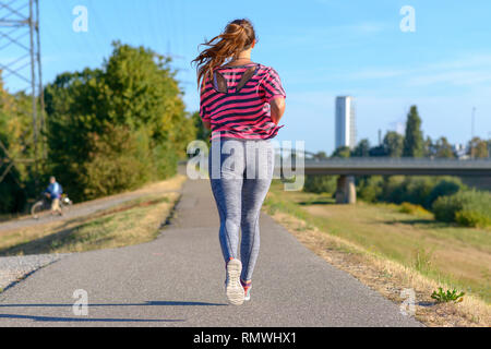 Vue arrière du young woman wearing sportswear courir le long de la rivière Banque D'Images