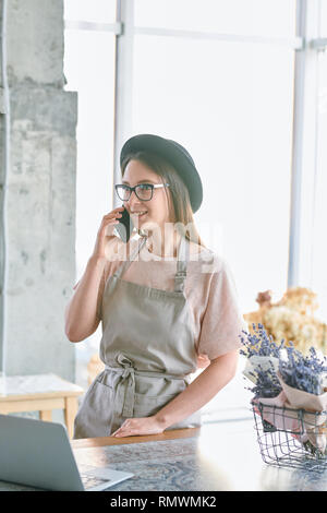 Jeune Femme au chapeau et vêtements de la consultation des clients sur smartphone tout en travaillant dans un fleuriste Banque D'Images