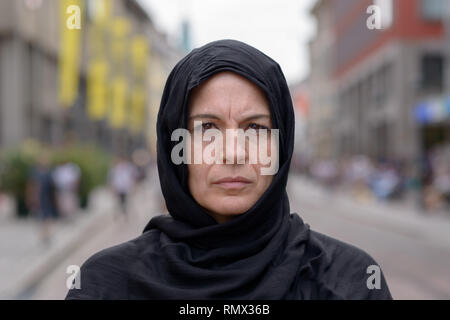 Femme musulmane portant un foulard ou voile dans une rue urbaine fixant pensivement à l'appareil photo dans un close up head and shoulders portrait Banque D'Images