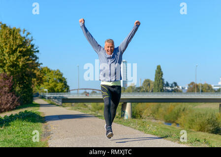 Happy fit acclamer l'homme d'âge moyen et à célébrer comme il marche le long d'un chemin rural à travers un parc verdoyant après le jogging Banque D'Images