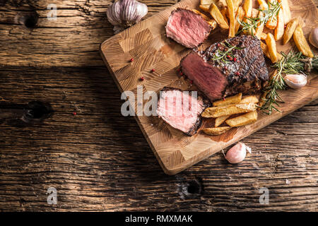 Pavé de boeuf grillé avec des pommes de terre frites sur planche de bois. Banque D'Images