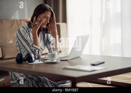 Les jeunes épuisé et inquiet femme travaillant à la maison avec un ordinateur portable Banque D'Images