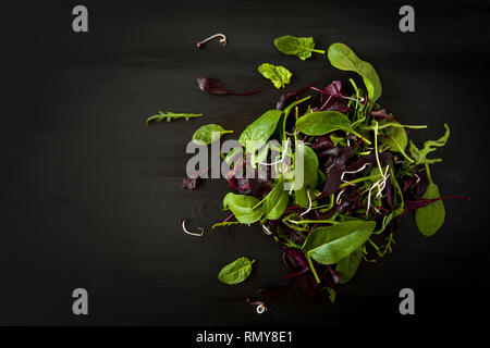 Detox de printemps mélange Salade de roquette, betterave, épinard et pousses sur planche de bois sombre sur fond noir, vue du dessus. Banque D'Images