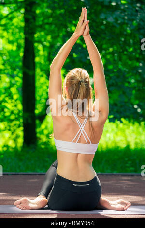 Fille mince coach pratique le yoga dans un parc d'été, vue de l'arrière Banque D'Images